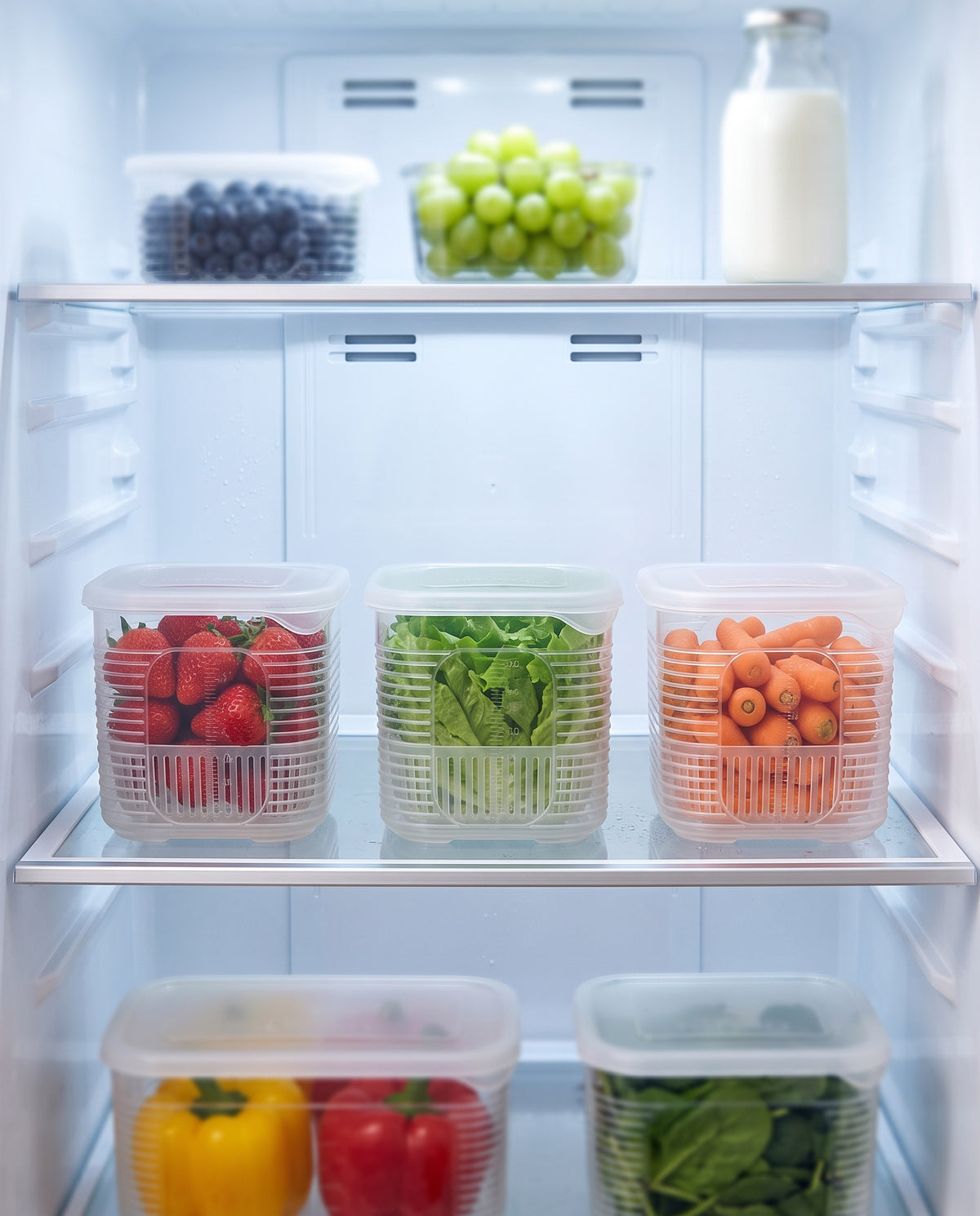 Clear fridge storage boxes with drain tray holding strawberries, grapes, blueberries and carrots